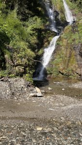 A scenic view of a waterfall cascading down rocky terrain, surrounded by lush green foliage.