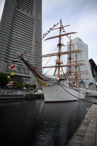 



A tall ship with raised sails docked between modern buildings, with Landmark Tower in Kanagawa, Japan.