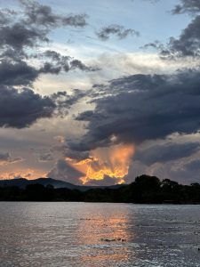 A stunning sunset scene over a calm lake, with the sun&#039;s rays piercing through dramatic clouds on the horizon. 