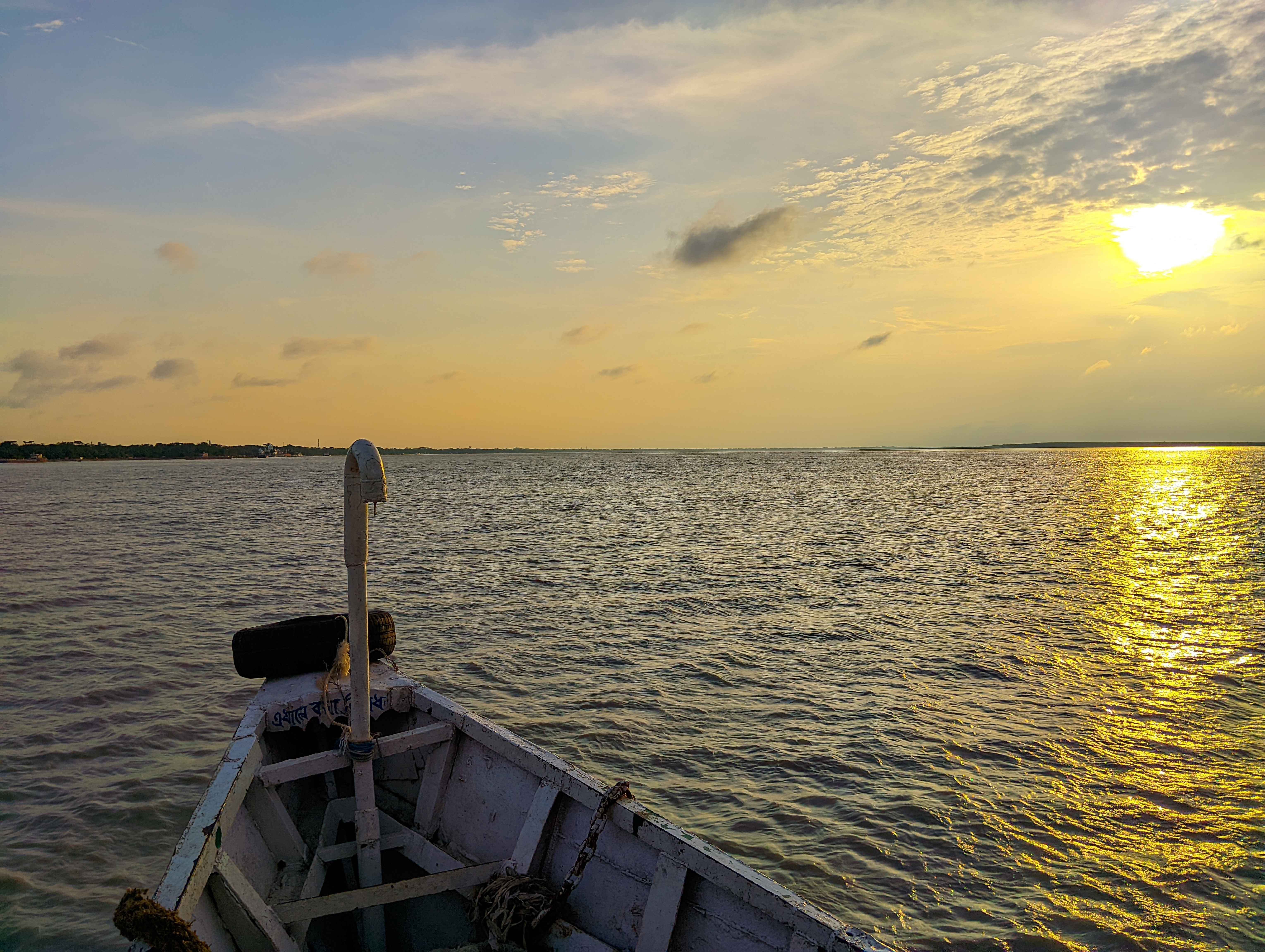 A calm river at sunset viewed from the front of a wooden boat, with golden sunlight reflecting on the water