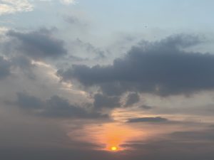 A sunset scene featuring a glowing orange sun partially obscured by clouds in the sky.