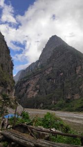 A breathtaking mountainous landscape featuring steep, rugged cliffs rising dramatically towards a cloudy sky.