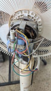 Close-up of an electric fan’s internal components, showing the motor, wiring, and connections.