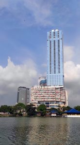 A tall, modern skyscraper with a glass façade stands prominently against a backdrop of partly cloudy blue sky in Sri Lanka
