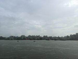 Rain falls over a wide river with two small boats and a busy city harbor in the distance.