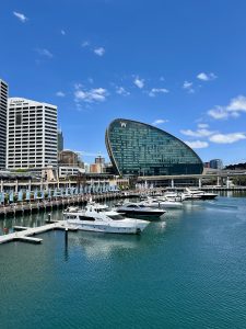 A ships is docked in a bustling harbor with the iconic W-shaped building towering behind it!