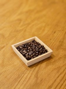 A small wooden tray filled with dark roasted coffee beans sits on a smooth wooden table in Kozhikode, Kerala. The warm tones make the beans look rich and fresh. 
