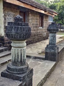 Two carved stone pillars stand at the entrance to an old structure near the Elephanta Caves, Mumbai, with detailed traditional designs and weathered textures.