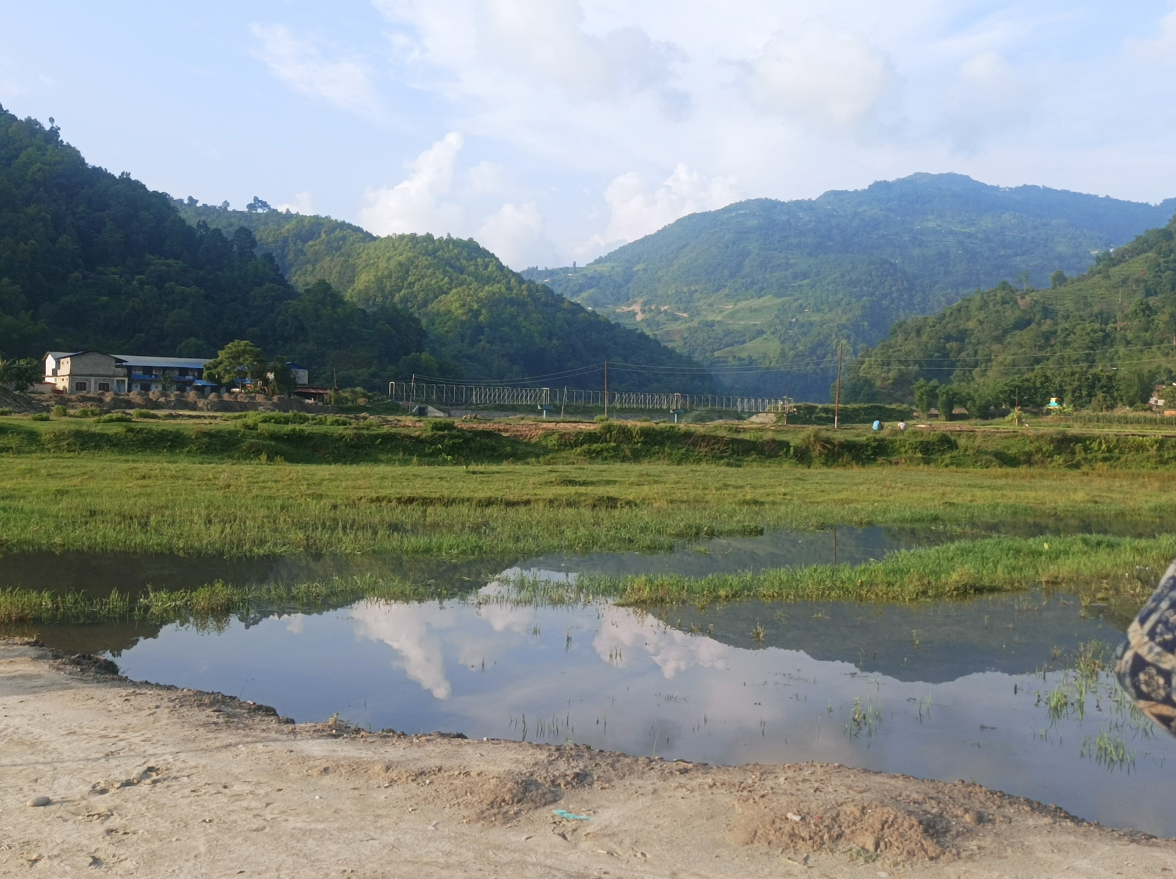 A scenic landscape featuring a reflection of fluffy white clouds in a small waterbody in the foreground.