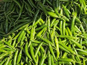 Close-up of shiny green chilies neatly arranged for sale at a vegetable market
