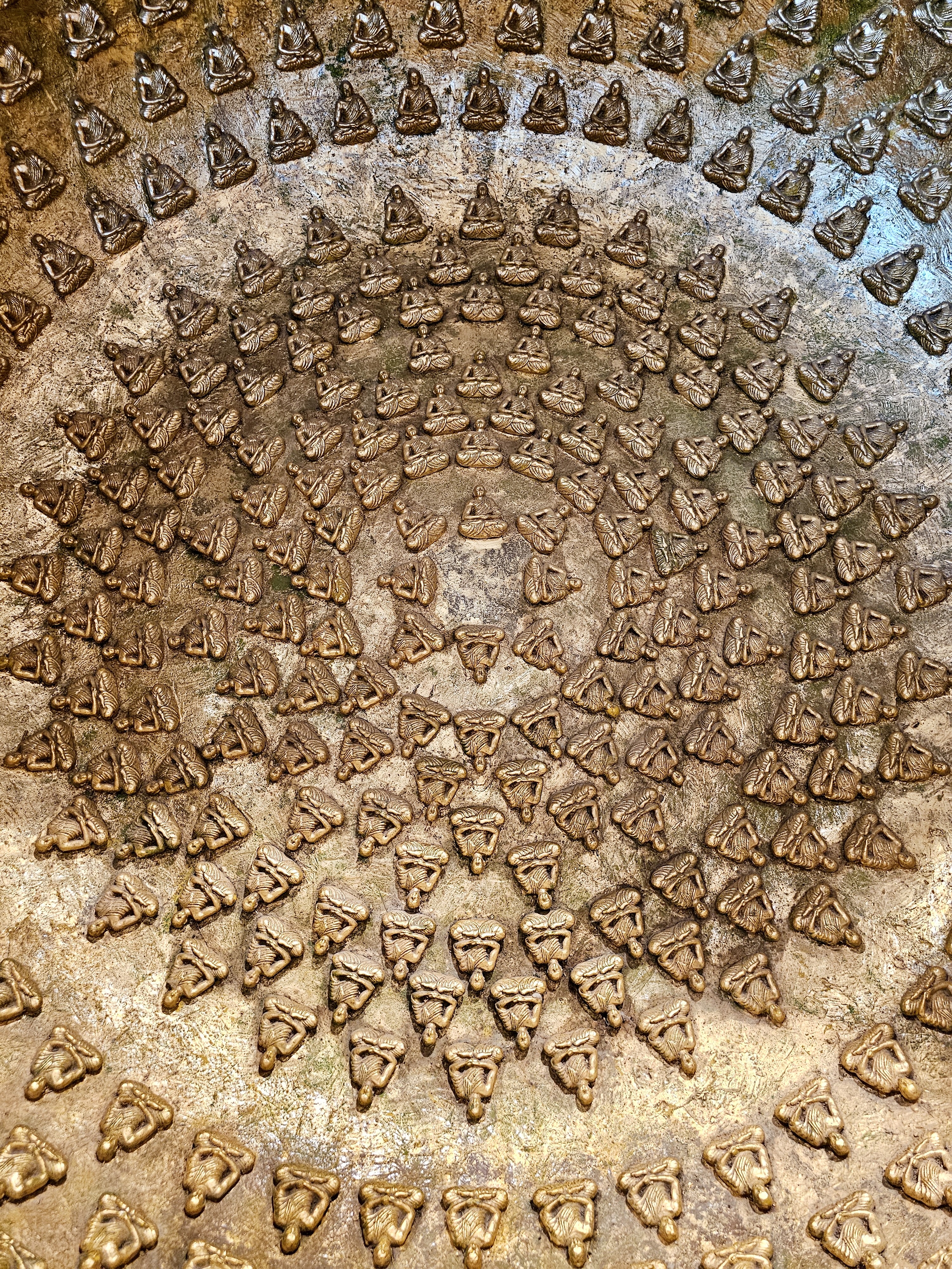 A detailed golden artwork showing many small Buddha figures arranged in circular patterns. A rich and intricate design seen in BKC, Mumbai. 