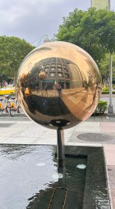 A large, reflective golden sphere stands on a pole near a shallow water feature. 