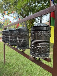 A row of traditional prayer wheels made of metal, adorned with intricate carvings and inscriptions, is displayed on a sturdy metallic frame.