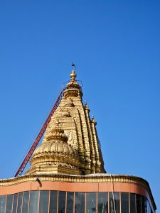 Golden temple gopuram (tower) with carvings and a clear blue sky in the background, located in Asalpha, Mumbai, Maharashtra. 