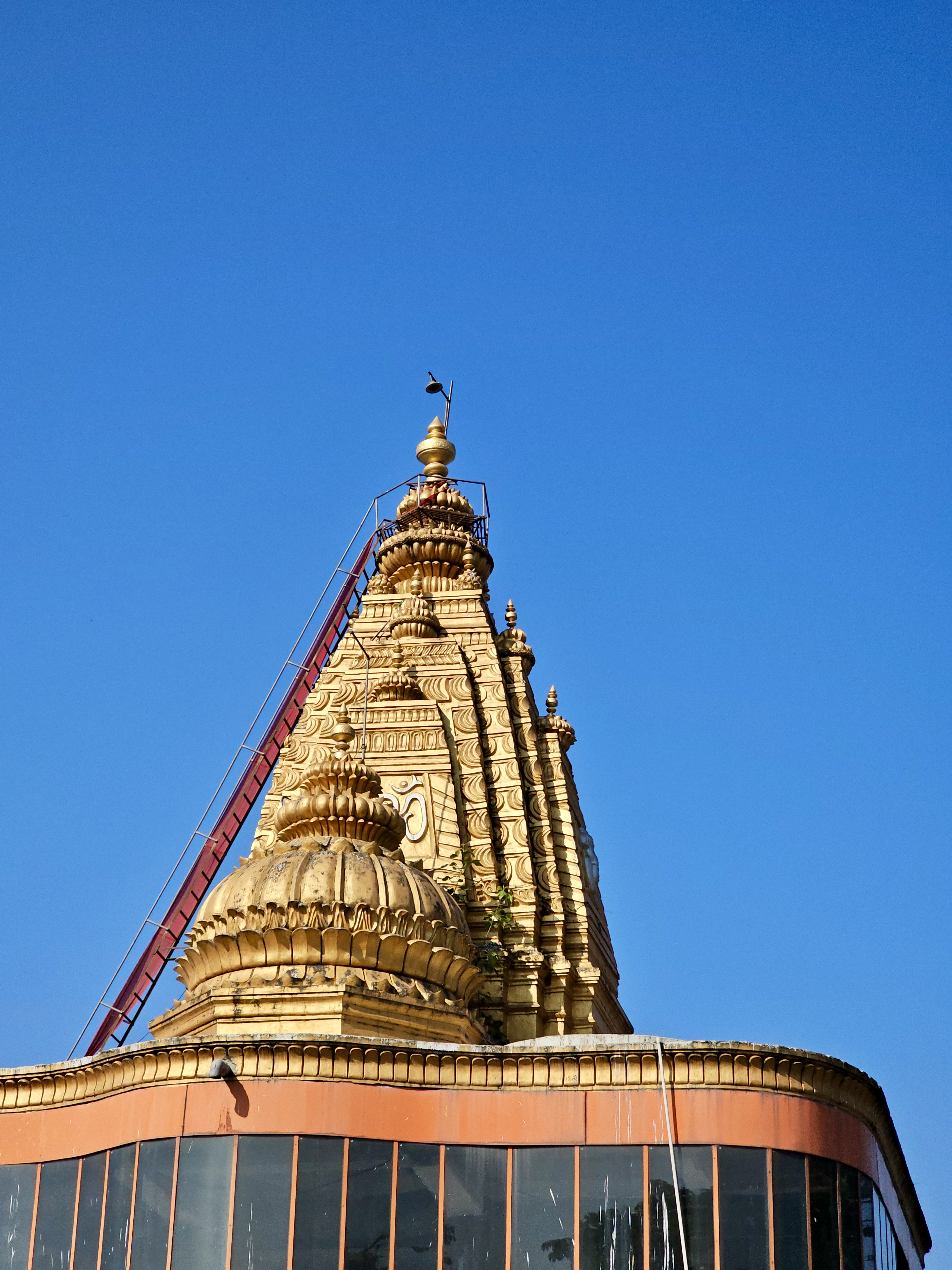 Golden temple gopuram (tower) with carvings and a clear blue sky in the background, located in Asalpha, Mumbai, Maharashtra.