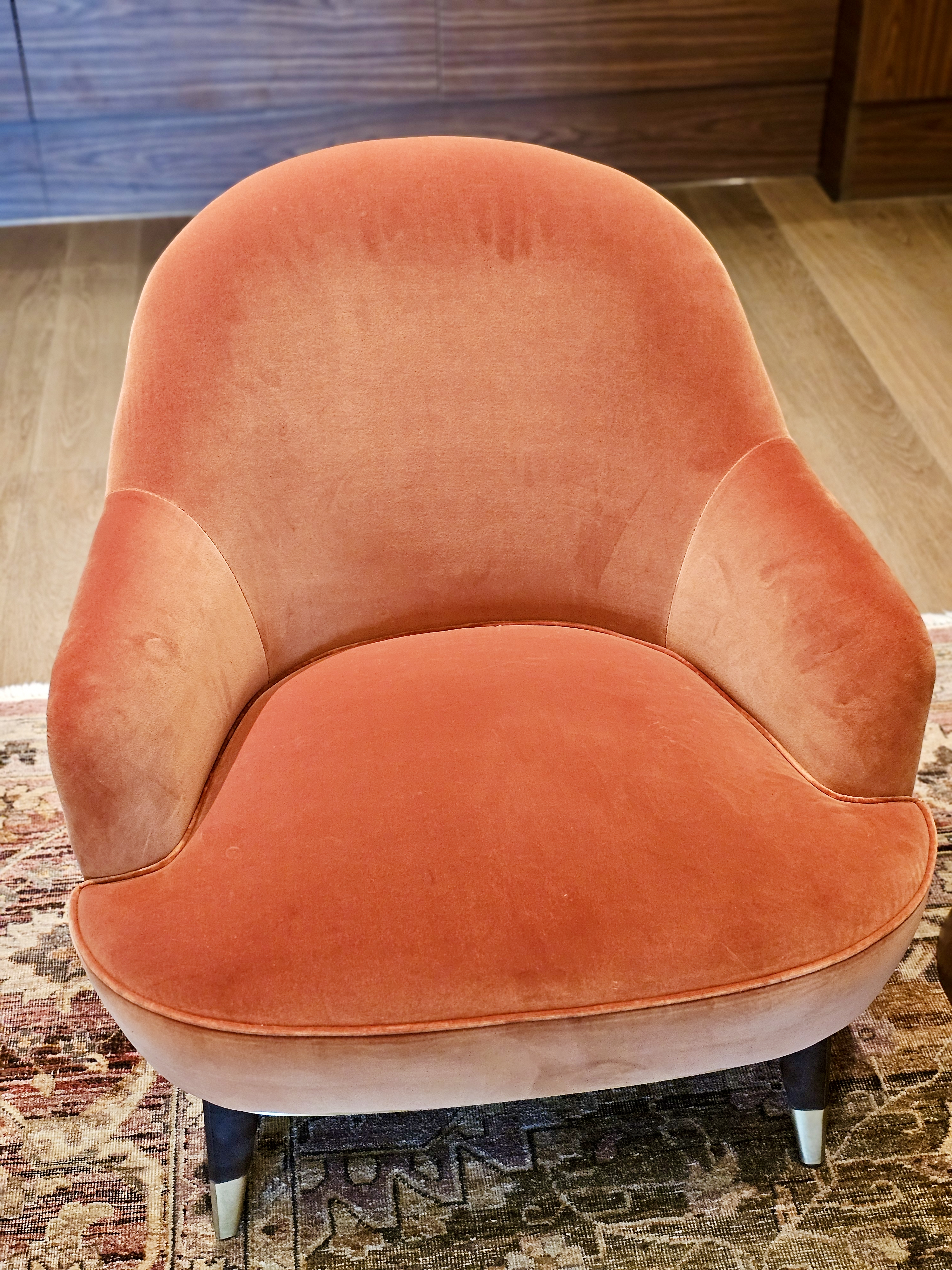 A soft orange velvet chair with curved arms and a cozy shape, placed indoors at BKC, Mumbai. The warm color and texture give it a welcoming look. 