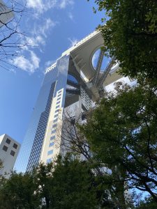 A modern skyscraper with a circular opening at the top rises against a clear blue sky. Osaka, Japan.