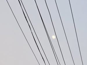 A bright full moon shines through a pattern of power lines stretched across the dusky sky in an evening scene from Cherupa, Kozhikode, Kerala. 
