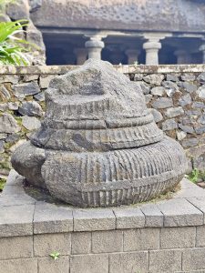 A large, weathered stone sculpture with layered carvings sits on a raised base, highlighting ancient craftsmanship at the Elephanta Caves, Mumbai. 