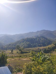 A panoramic landscape featuring rolling mountains in the background under a clear blue sky.
