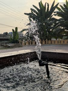 A close-up view of a water fountain spraying water into the air, with droplets shimmering in the sunlight.