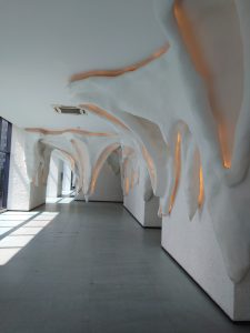 The image features a white ceiling illuminated by orange lights. It showcases an indoor setting, likely within a building, where the ceiling adds to the overall ambiance of the space. The artistic element is emphasized through the use of color and design.
