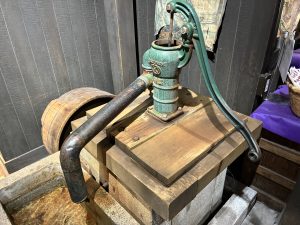 A vintage hand water pump sits on a wooden platform. 