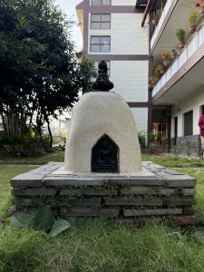 A small white structure with a dome shape sits on a stone base, featuring a black entrance where a statue of Buddha is visible. 