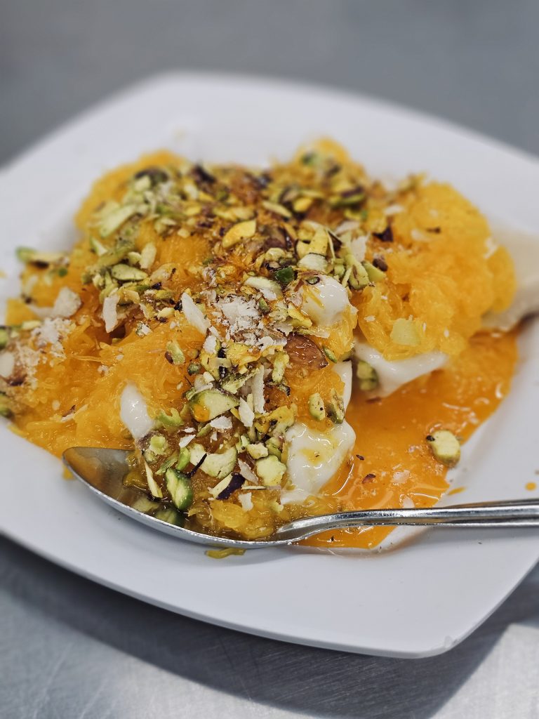 A Kesar Kulfi dessert topped with chopped pistachios, photographed in Perumanna, Kozhikode. Warm colours and textures make it look delicious.