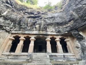 The impressive front of a rock-cut temple with sculpted stone columns carved into a hill. Taken at Elephanta Caves, Mumbai, Maharashtra.