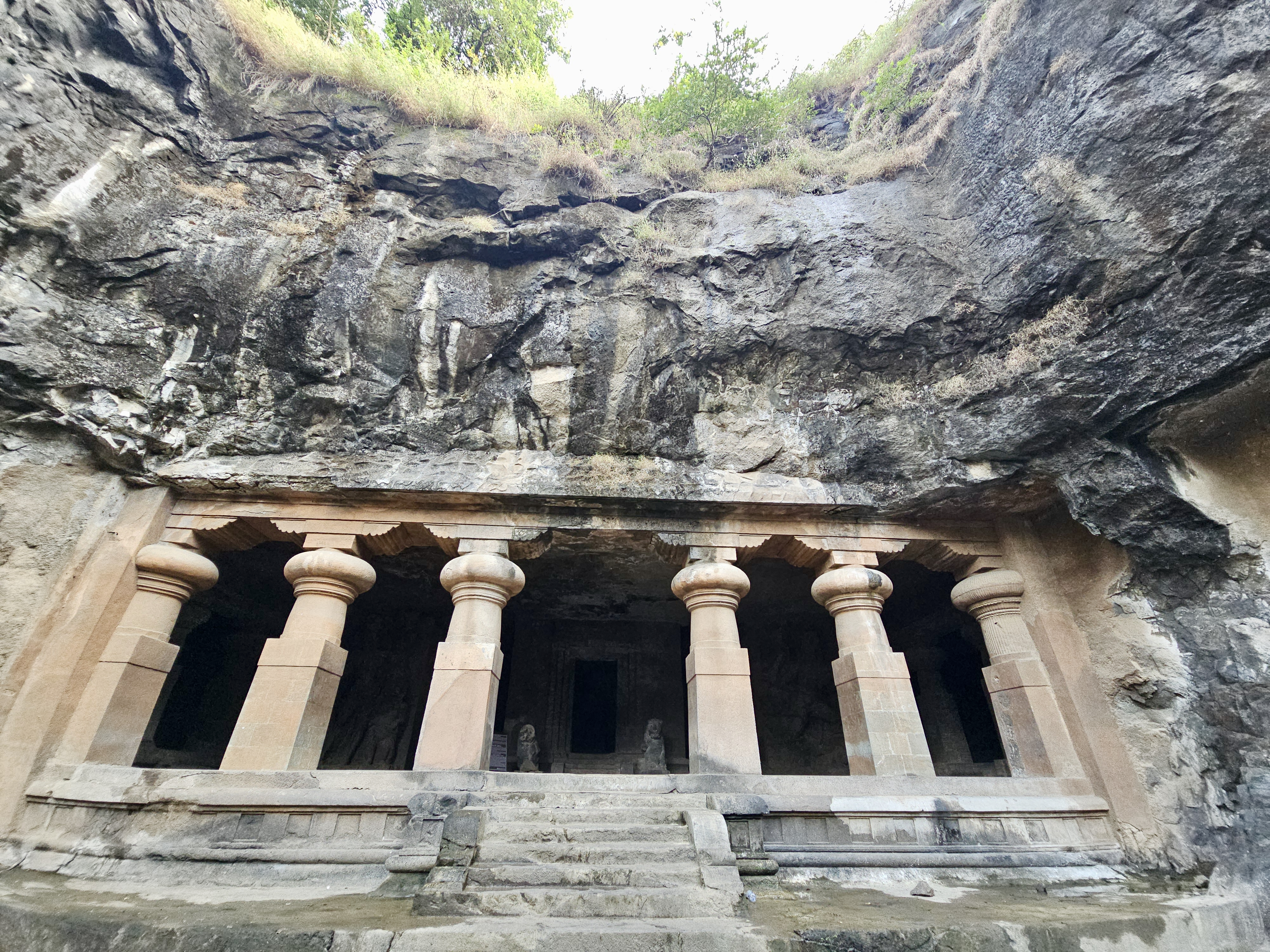 The impressive front of a rock-cut temple with sculpted stone columns carved into a hill. Taken at Elephanta Caves, Mumbai, Maharashtra.