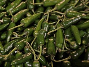 A heap of fresh green chilies is displayed together, their glossy texture and curved shapes highlighting their natural appearance. The photo was captured at a market in Kozhikode, Kerala.
