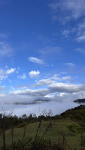A scenic view featuring a bright blue sky with scattered clouds above a misty landscape.