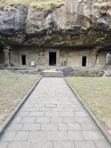 A straight stone path leads to the carved entrance of one of the Elephanta Caves in Mumbai, with two dark doorways set into the rocky hillside. 