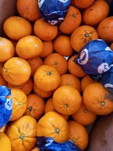Bright orange oranges in a fruit box, some covered in blue wrapping paper. Taken in Perumanna, Kozhikode, Kerala.