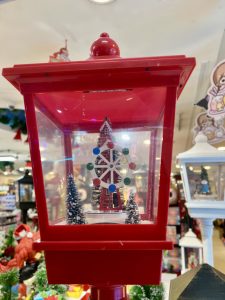 A decorative red lantern-style snow globe contains a miniature Ferris wheel and two small, snow-dusted evergreen trees.