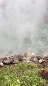 A misty landscape featuring a stream of steam rising from the ground, surrounded by rocks of various colors.