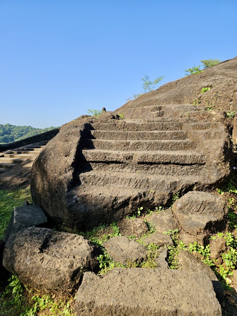 Rock-cut steps leading up the slope at Kanheri Caves in Borivali, Mumbai, are highlighted by sunlight and surrounded by patches of greenery.