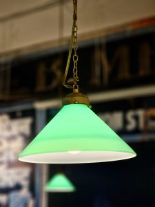 A bright green hanging lamp is glowing warmly in a soft indoor light. Its simple shape stands out against the blurred background at BKC, Mumbai. 
