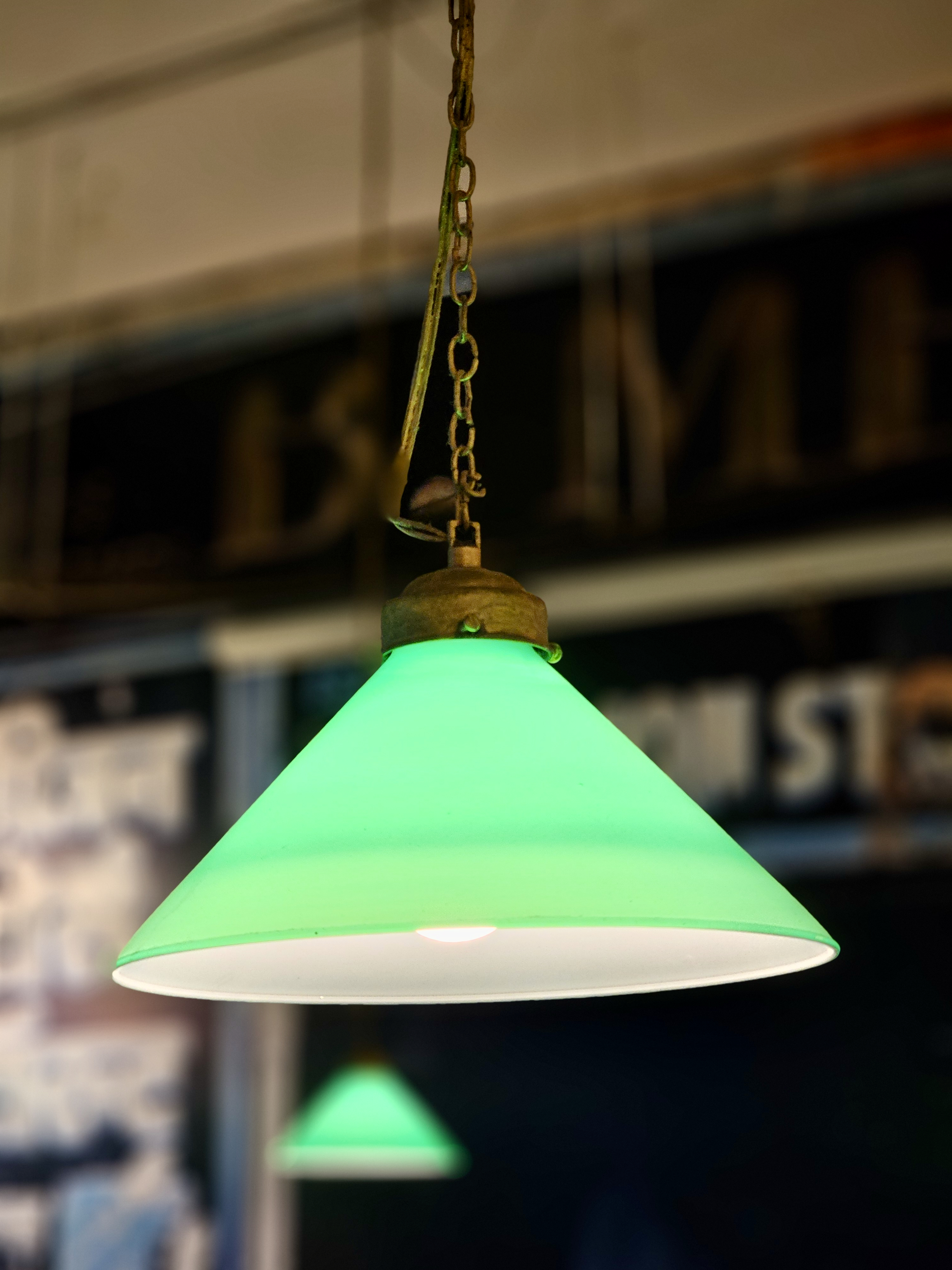 A bright green hanging lamp is glowing warmly in a soft indoor light. Its simple shape stands out against the blurred background at BKC, Mumbai.