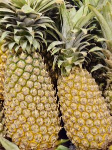 Fresh pineapples with golden skin and leafy crowns stacked together at a hypermarket in Kozhikode, Kerala. Their textured surface and rich color show perfect ripeness. 