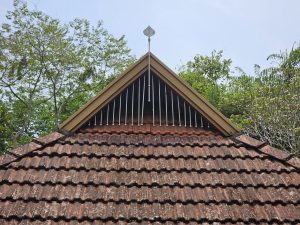 A traditional tiled roof of a small temple with an open vent under the top ridge. The wooden frame and metal rods add a simple design detail, photo taken in Wandoor, Kerala. 