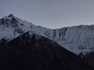 A panoramic view of rugged mountain peaks covered in snow, with a darker, rocky mountain range in the foreground.