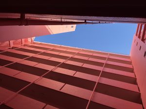 ピンクのマンションの吹き抜けから青空を眺める　/　Gazing at the blue sky from the atrium of the pink apartment building