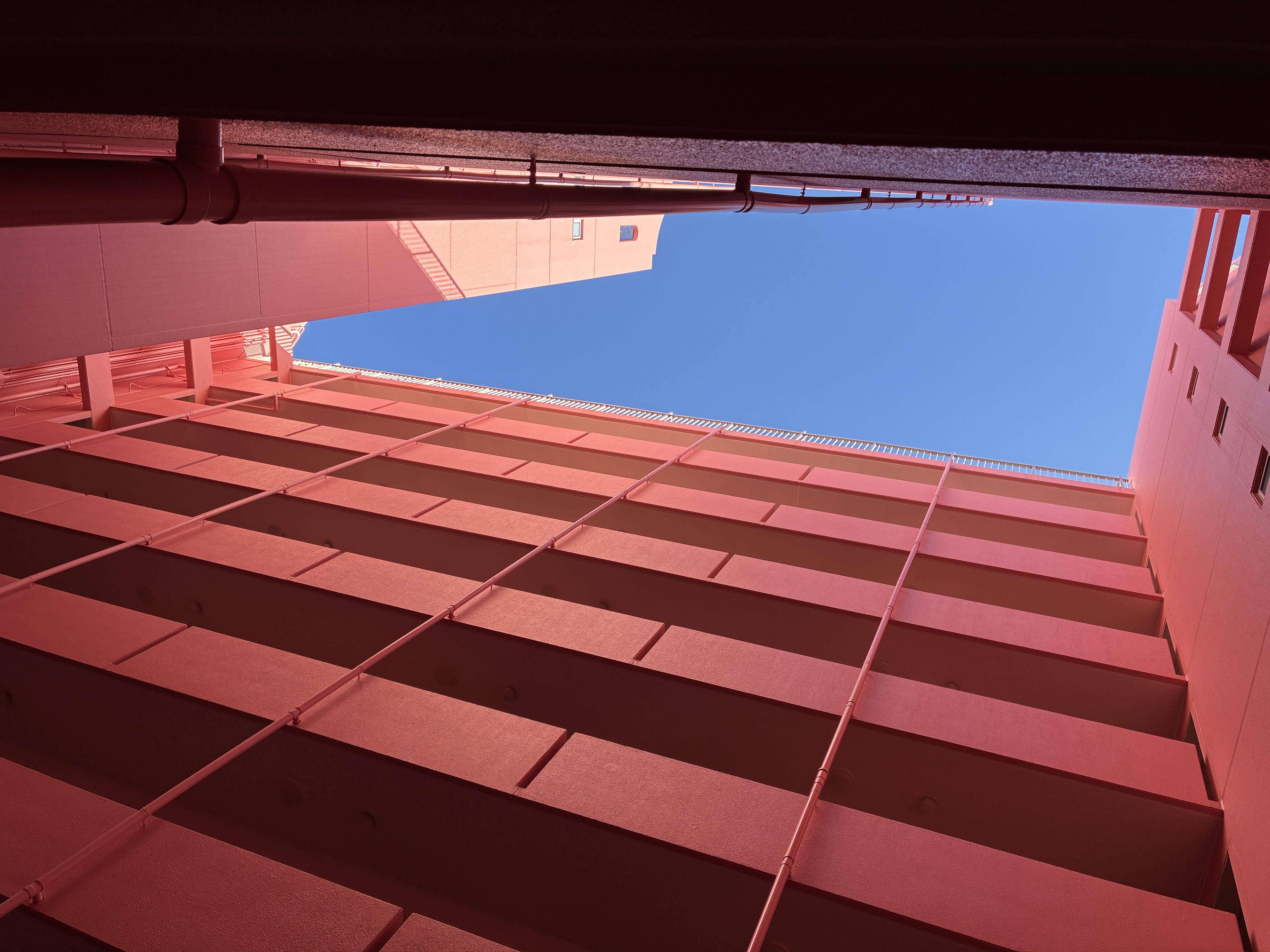 ピンクのマンションの吹き抜けから青空を眺める　/　Gazing at the blue sky from the atrium of the pink apartment building