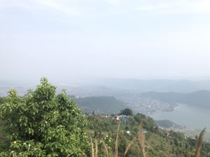A panoramic view from a hillside overlooking a valley, with a serene lake and a distant town visible in the background. 