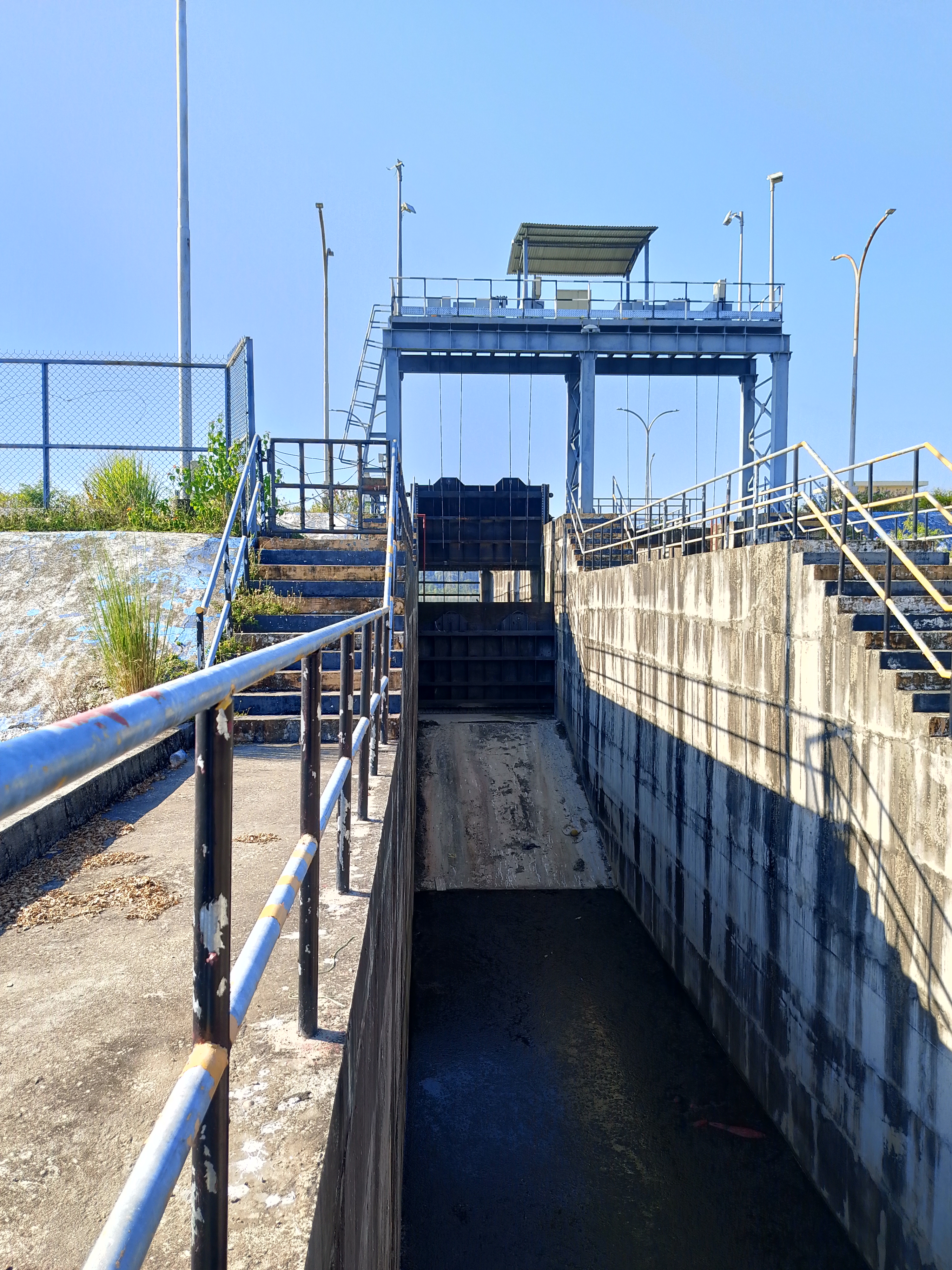 A water management structure with concrete walls and metal railings leads down to a canal. 