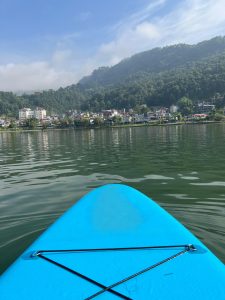 A view from a paddleboard on calm water, featuring a bright blue paddleboard in the foreground. 