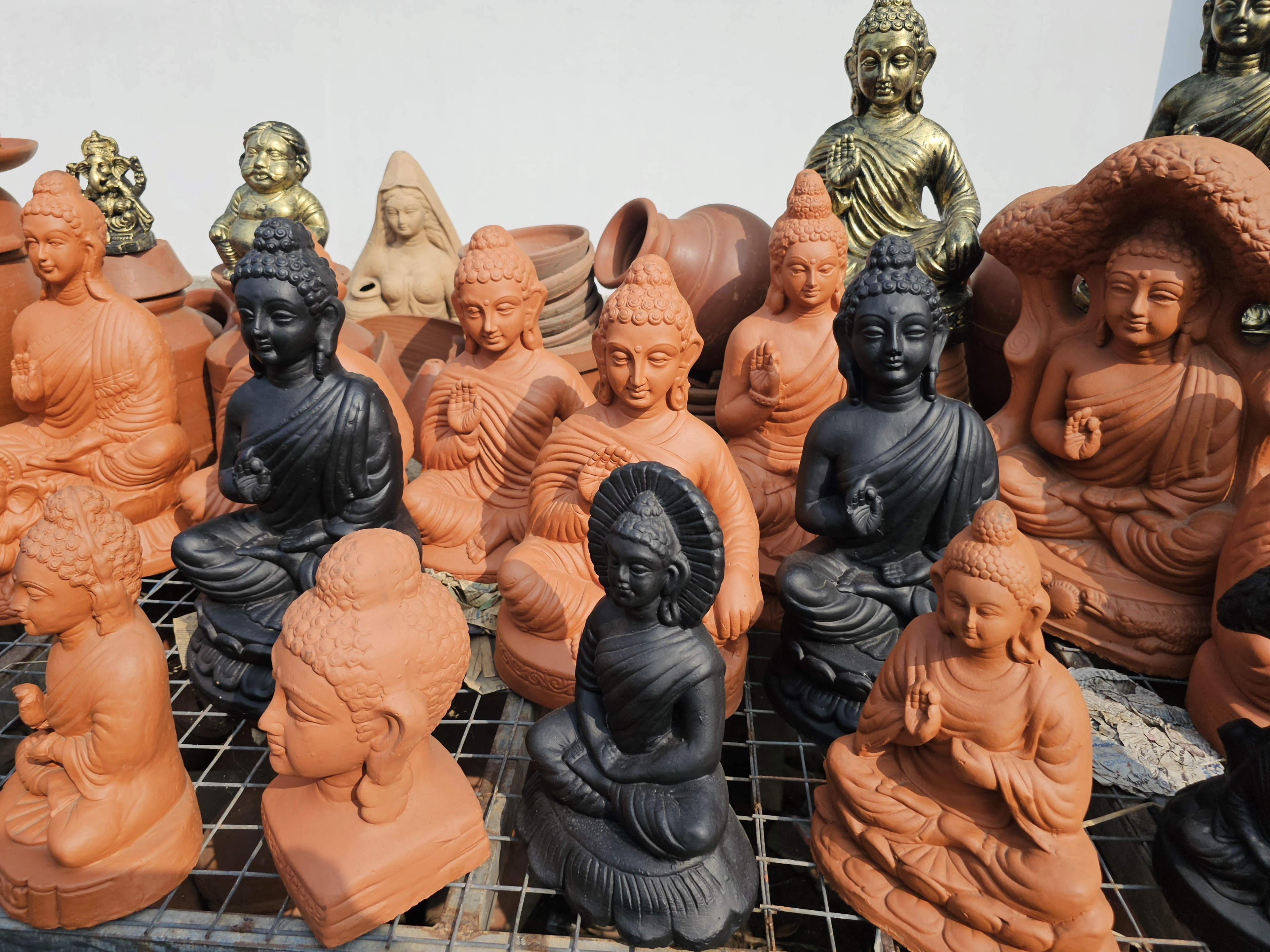 A group of clay Buddha statues in different colors is arranged on a street in Kozhikode, Kerala. The statues exhibit calm expressions and intricate handwork, featuring traditional designs. 