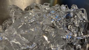 A closeup of a cluster of ice cubes all frozen together. Light sparkles through, including a blue light.
